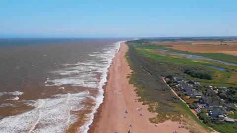 Waves crash onto wide sandy beach under clear blue sky. Fields stretch beyond Stock Footage 342025478