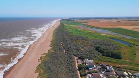Waves crash onto wide sandy beach under clear blue sky. Fields stretch beyond Stock Footage 342025528