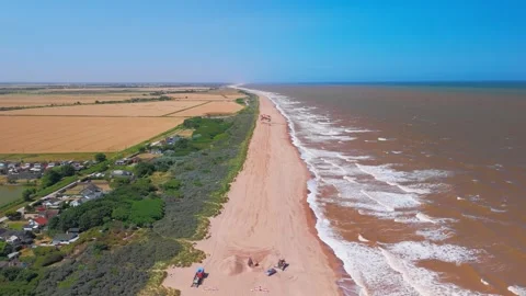 Waves crash onto wide sandy beach under clear blue sky. Fields stretch beyond Stock Footage 342025548