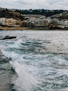 Waves crashing against pier create stunning contrast with coastal city in 스톡 사진