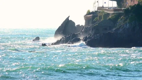 Waves crashing against the rocky cliffs of the coast on a sunny day, along t Stock Footage 293362569