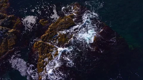 Waves crashing against rugged rocks at the coast during a bright sunny day Stock Footage 332065717