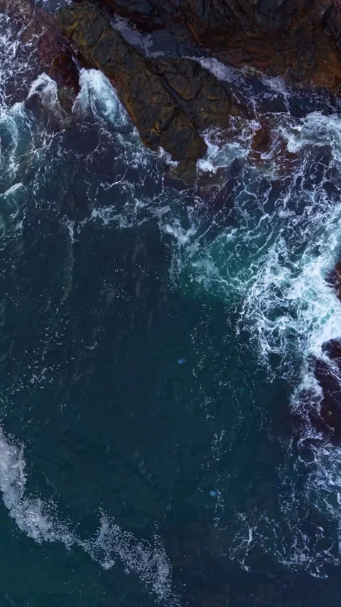 Waves crashing against rugged rocks showcase the beauty of nature along a Stock Footage 332094777