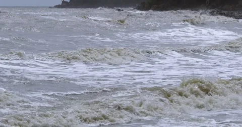 Waves crashing against rugged rocks along coastline beneath dramatic cloudy sky Stock Footage 345282120