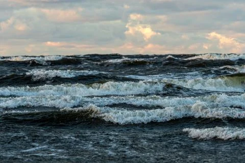 Waves crashing on a beach under a cloudy sky during sunset Stock Photos