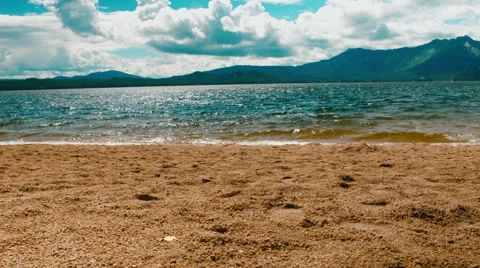 Waves crashing gently on quiet sandy beach. mountain background. 4K footage Stock Footage 64861275