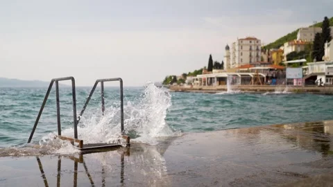 Waves crashing on land at empty stairset into sea with Mediterranean Town Stock Footage 277720584
