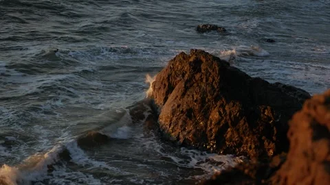Waves crashing on a large rock during golden hour Video stock 246389664