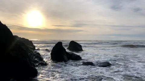 Waves Crashing Over Pointed Rocks In Ocean With Sun Beaming Through Cloudy Sky Stock Footage 234005802