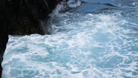 Waves crashing over rugged black volcanic rocks, creating white foam, splashes Stock Footage 346649146