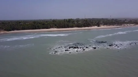 Waves crashing on rocks with beach, trees and buildings in background Stock Footage 208937032