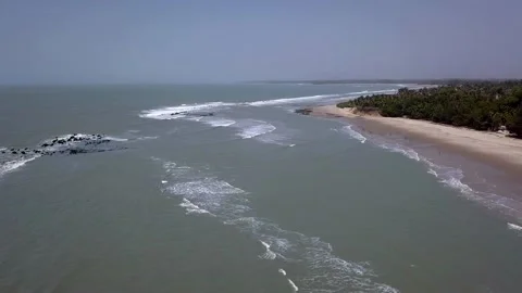 Waves crashing on rocks with beach, trees and buildings in background Video stock 208937039