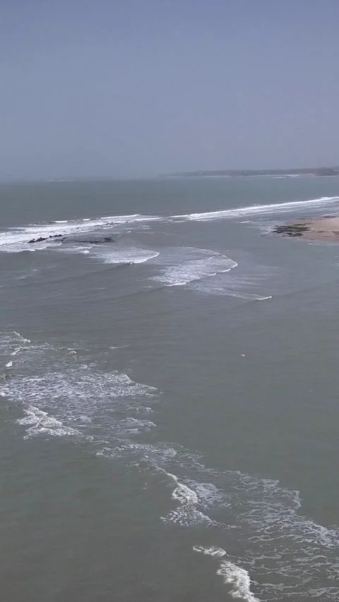 Waves crashing on rocks with beach, trees and buildings in background Stock Footage 230671515