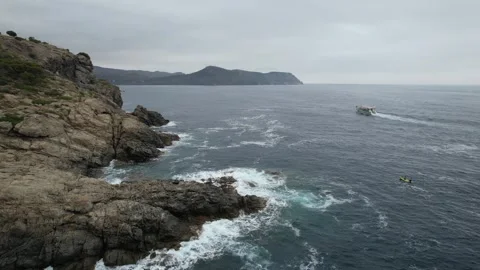 Waves crashing on rocks with distant boat drone view in Punta Falconera Stock Footage 294197814
