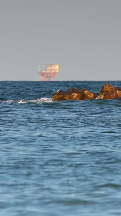 Waves crashing onto rocky shore with distant ship Stock Footage 345998824