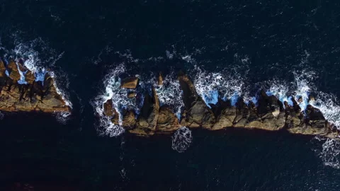 Waves crashing on rugged rocks along the coastline at sunset revealing the Stock Footage 331984911