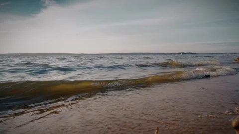 Waves crashing on sandy beach at sunset with sailboats in background Stock Footage 292868843