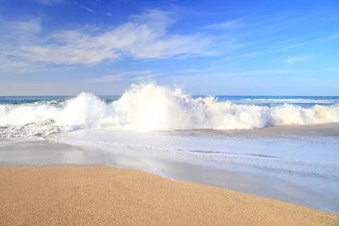 Waves crashing on sandy beach under blue sky Stock Photos