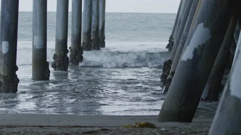 Waves crashing underneath pillars of pier in Santa Monica, California in evening Stock Footage 211799776