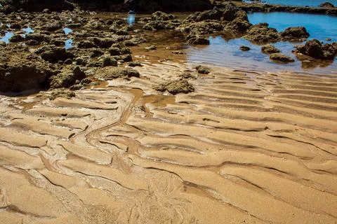 Waves create patterns on the sand at Praia dos Arrifes in Albufeira, Portugal Photos