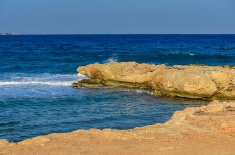 Waves dance against rugged cliffs under a clear blue sky at coastal serenity Stock Photos