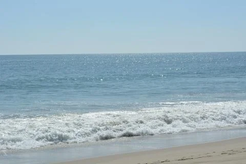 Waves Dance Gently on the Shore Under a Bright Blue Sky at Midday Stock Photos