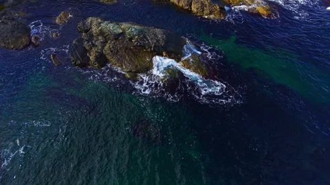 Waves dance gracefully around rugged rocks in a shimmering seascape at the break Stock Footage 332072947