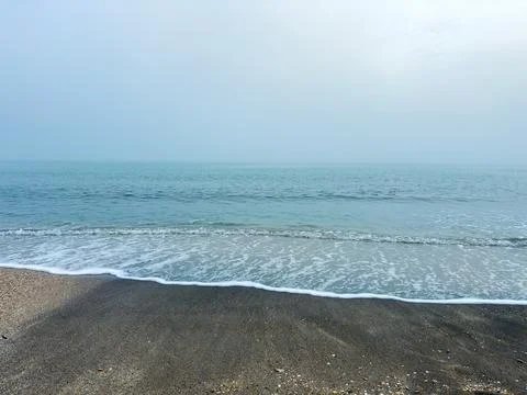 Waves flow softly onto the sand at a beach. The sky is gray and cloudy, and t Stock Photos