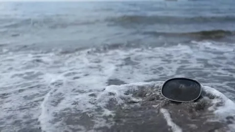 Waves flowing over recreational diving mask lying on beach sand by sea Stock Footage 292950063