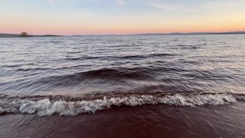 Waves gently break on a Swedish lake at sunset, bathed in orange light. Stock Footage 276188253