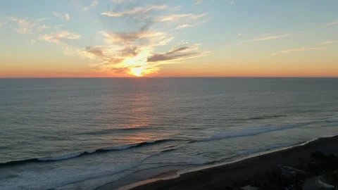 Waves gently breaking along dark sandy beach as the sun sets on the horizon Video stock 319625816