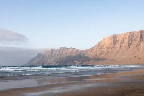 Waves gently crash on a sandy beach with cliffs in the background at sunset Stock Photos