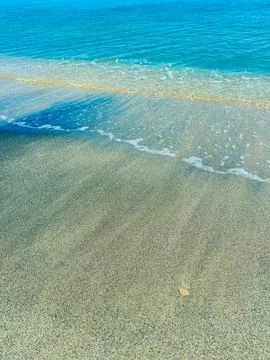 Waves gently flow onto the shore, creating smooth patterns in the sand as a s Stock Photos
