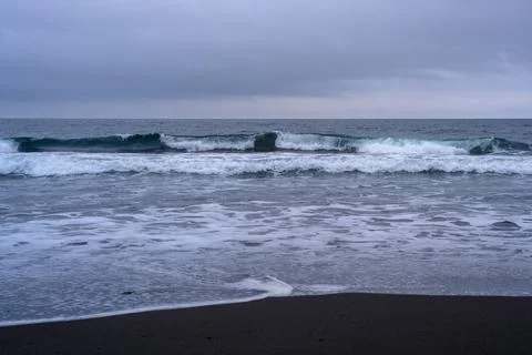 Waves gently lap against the black sandy beach under an overcast sky in Russi Stock-Fotos