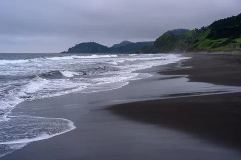 Waves gently lap against the dark sands of a quiet beach in Russia Stock Photos