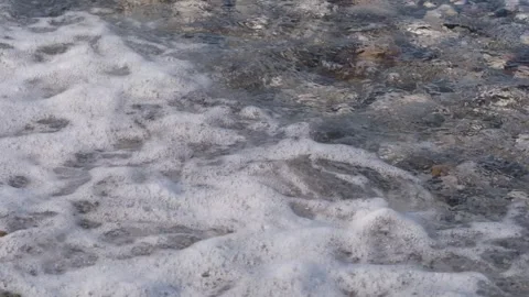 Waves gently lap against a rocky shoreline, creating foam and bubbles over Stock Footage 345843302