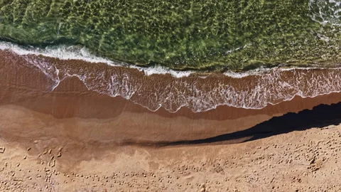 Waves gently lap against the sandy shore as footprints mark the warm beach, Stock Footage 331974108