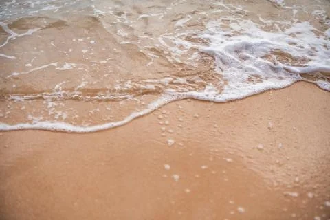 Waves gently lap against a sandy shore at sunset on a tranquil beach Stock Photos