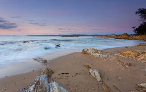 Waves gently lap the quiet beach at dawn Stock Photos