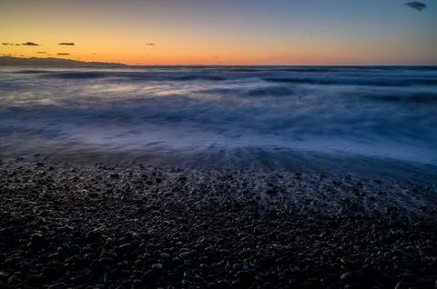 Waves gently lap the rocky shore as dusk settles over the tranquil ocean la.. Stockfoto's