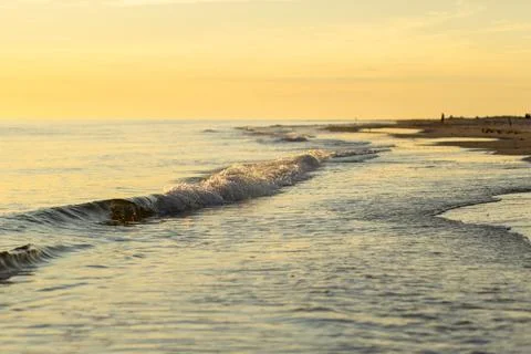 Waves gently lap the shore at sunset, creating a serene atmosphere along the Stock Photos
