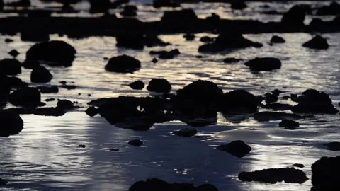 Waves gently lapping over a rocky beach at sunset, long lens Stockbeeldmateriaal 165280069