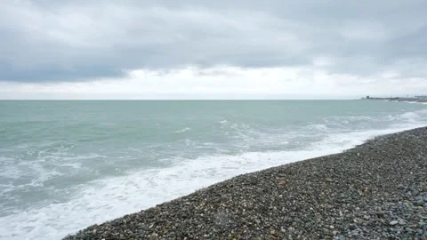 Waves gently lapping on a pebbly beach under an overcast sky Stock Footage 295230776