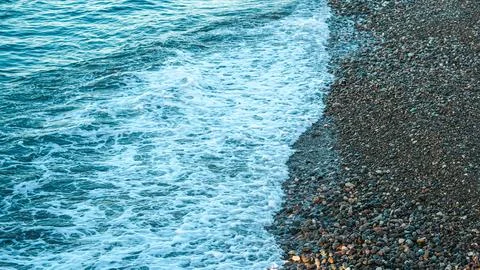 Waves gently lapping on rocky beach shoreline with clear blue water Stock Photos
