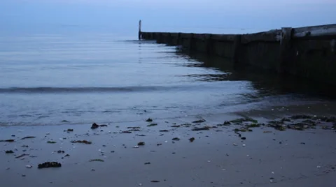Waves gently lapping at the shore and a wooden jetty at dusk on a beach Stock Footage 39535488