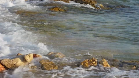 Waves gently roll in and crash on the rocky beach on clear sunny day. Stock Footage 298564617