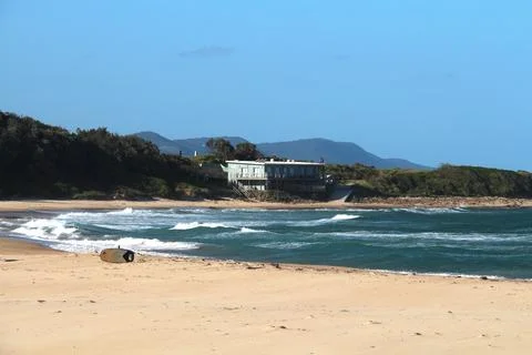 Waves gently roll onto a sandy beach with a house in the background on a cl.. Stock Photos