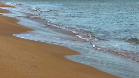 Waves gently roll onto the shore at a sandy beach during midday. Waves touch the Stock Footage 327158540