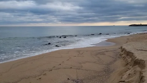 Waves gently rolling onto sandy beach under dramatic cloudy coastal sky Stock Footage 322124796
