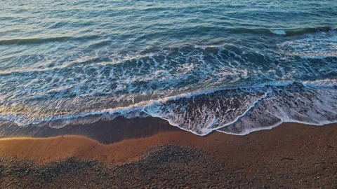 Waves gently rolling onto the sandy shore during sunset on a tranquil beach Stock Footage 290098029